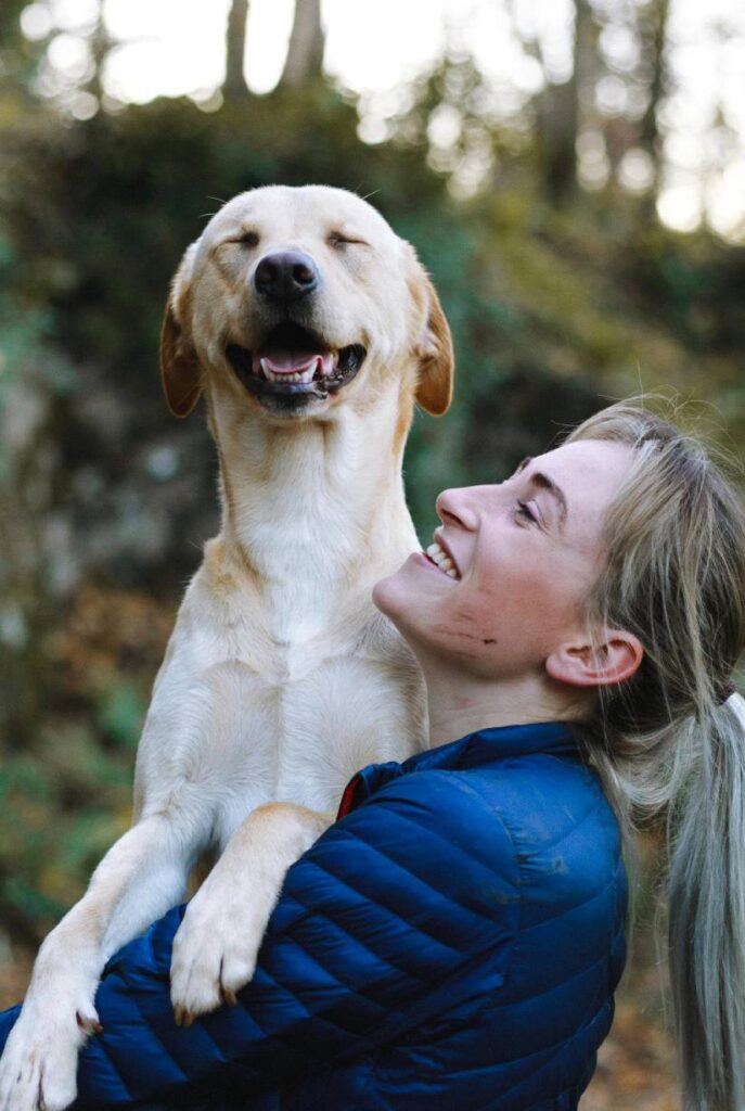 A golden retriever emotional support dog being held in its owner's arms while they are both smiling
