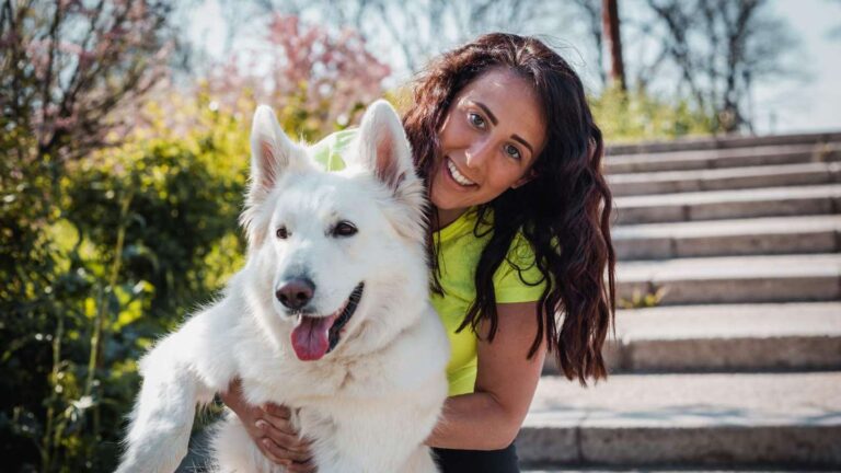 a woman smiling and hugging a happy white German shepherd while learning about the best mindset for dog training