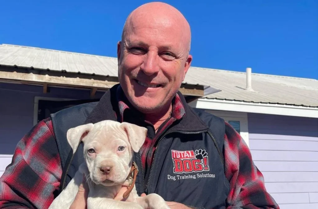 Brice Cavanaugh smiling while holding a happy white Pitbull puppy that is undergoing puppy training in Austin tx with Total Dog!